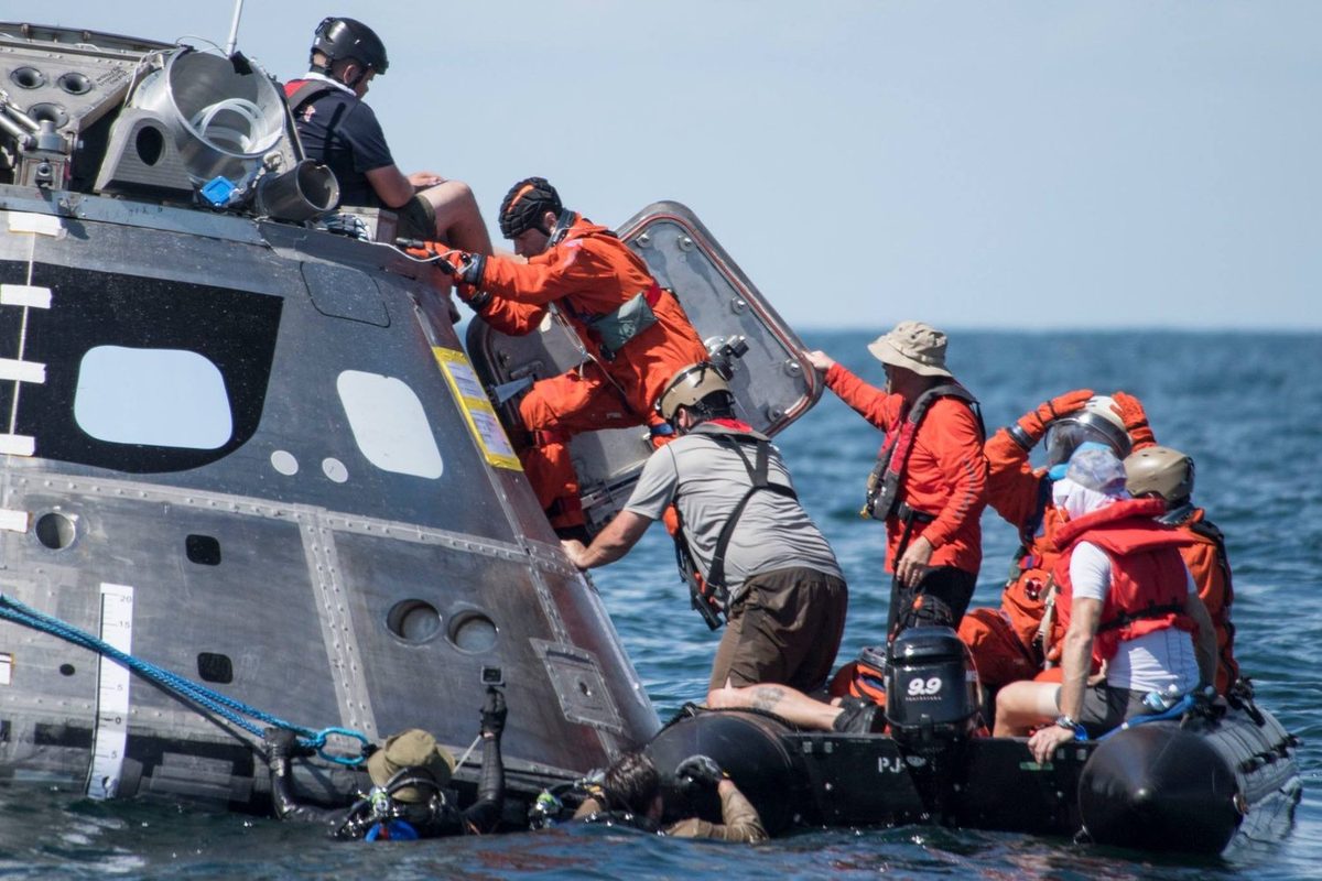 Astronautes en combinaison orange sortant de la capsule Orion flottante lors d’un essai en mer